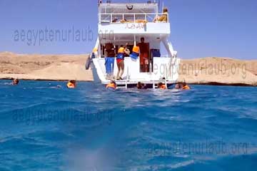Touristen die beim Schnorcheln an einem Riff bei Hurghada im Roten Meer in Ägypten über die Leitern am Heck der Yacht an Deck klettern.